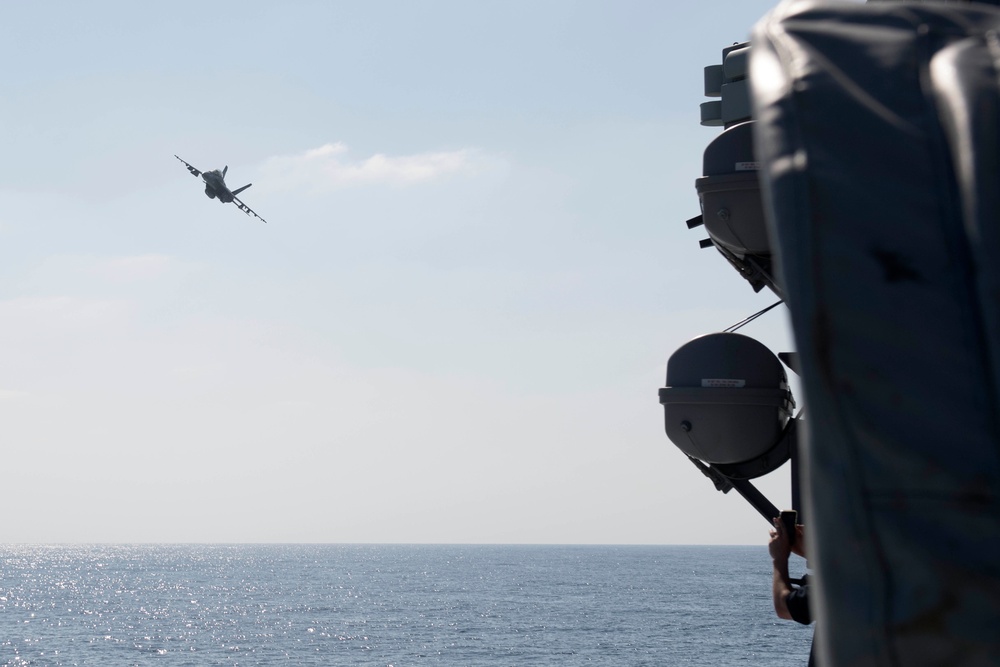 An F/A-18 Super Hornet, from the aircraft carrier USS John C. Stennis (CVN 74), flies by the guided-missile destroyer USS Spruance