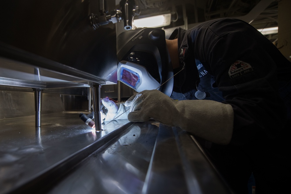 U.S. Navy Hull Maintenance Technician welds a coffee machine to a table aboard the guided-missile destroyer USS Stockdale