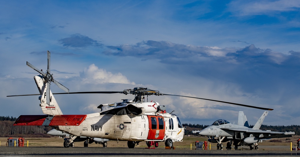 A MH-60S search and rescue helicopter sits near an EA-18G Growler.