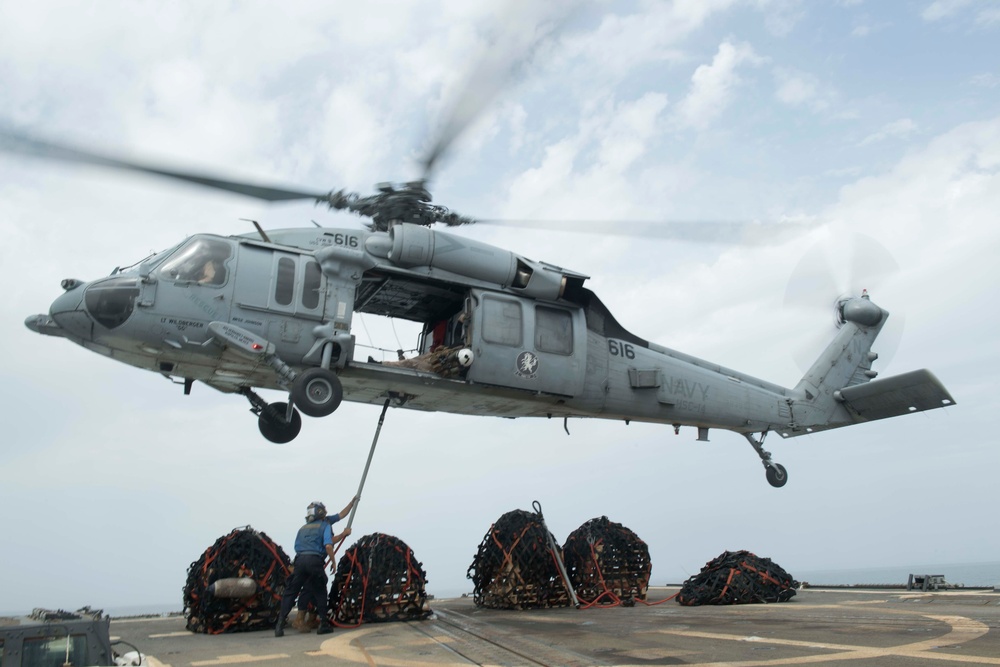 U.S. Sailors connects cargo to an MH-60S Sea Hawk on the flight deck of USS Spruance