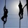 Balikatan 2019: U.S. Marines with 3/6 Interact with Philippine Marines Two individuals are silhouetted against a bright sky while climbing ropes between vertical poles, suggesting a physical training or obstacle course environment. The strong backlight from the sun creates a dramatic contrast, rendering both figures as dark silhouettes. The scene conveys physical exertion and athletic challenge.