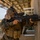 Balikatan 2019: Air Assault with 3rd Battalion, 6th Marines A soldier in MARPAT (Marine pattern) camouflage uniform is taking a tactical firing position against a concrete wall, aiming a rifle equipped with optics. At least two other military personnel are visible in the background. The setting appears to be a military training facility or urban operations exercise.