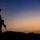 Balikatan 2019: Enjoying the sunrise A silhouetted figure stands against a twilight sky at dusk or dawn, holding what appears to be a military-style rifle. The person is wearing a wide-brimmed hat and is positioned in profile facing right. A mountain range and utility lines are visible in the background.
