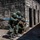 Balikatan 2019: 3/6 Room clearing drill, multi-national training with the AFP The image shows a group of military personnel conducting a training exercise at what appears to be a mock urban combat facility. Soldiers in camouflage uniforms are positioned along a stone block wall in tactical stances, aiming rifles fitted with blue training barrel inserts (Simunition/MILES gear indicators). The presence of blue-tipped training weapons confirms this is a simulated combat drill rather than a live operation.