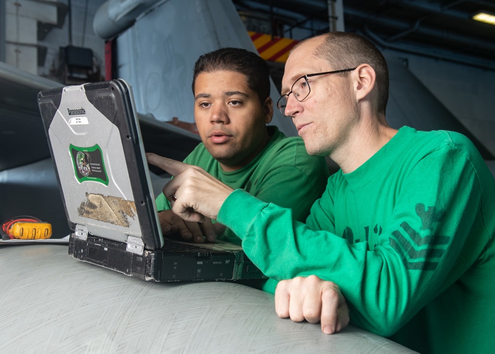 U.S. Sailors look at schematics for aircraft wiring