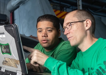 U.S. Sailors look at schematics for aircraft wiring