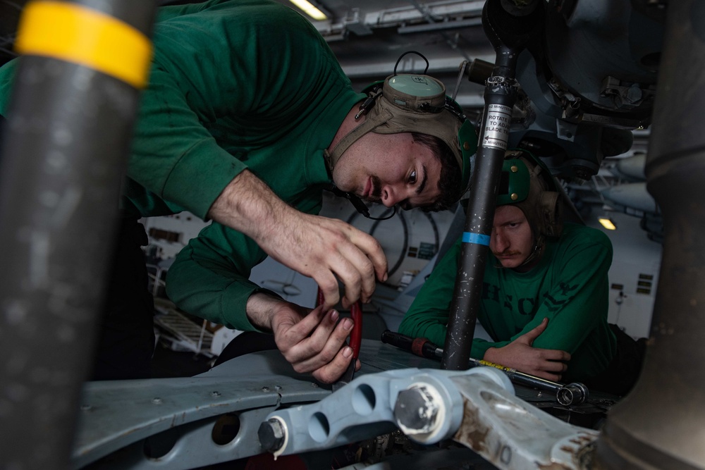 U.S. Sailors conduct maintenance on the scissors assembly of an MH-60S Sea Hawk