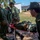 Humanitarian Mine Action increases demining capacity in Morocco A group of military personnel in olive green uniforms are conducting what appears to be a medical evacuation drill or training exercise. One soldier is lying on a red stretcher being transported by fellow soldiers across a gravel path. The setting appears to be a military base or training facility with a white building and construction equipment visible in the background.