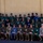 Humanitarian Mine Action increases demining capacity in Morocco A formal military group photograph featuring personnel from multiple nations in various uniforms, posed in three rows in front of a tan/beige building. The group includes individuals wearing US Marine Corps camouflage uniforms, dark navy/French-style naval uniforms, olive green uniforms, and blue uniforms, suggesting a multinational military exercise or training event. An American flag and what appears to be a red flag are visible on the left side of the image.