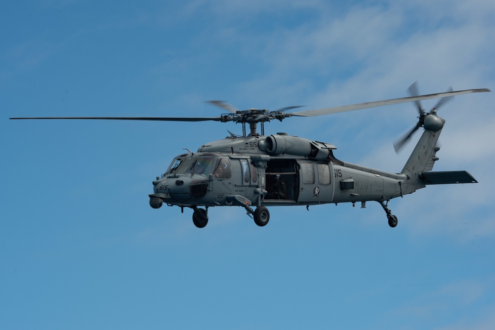 An MH-60S Sea Hawk flies alongside the aircraft carrier USS John C. Stennis (CVN 74)