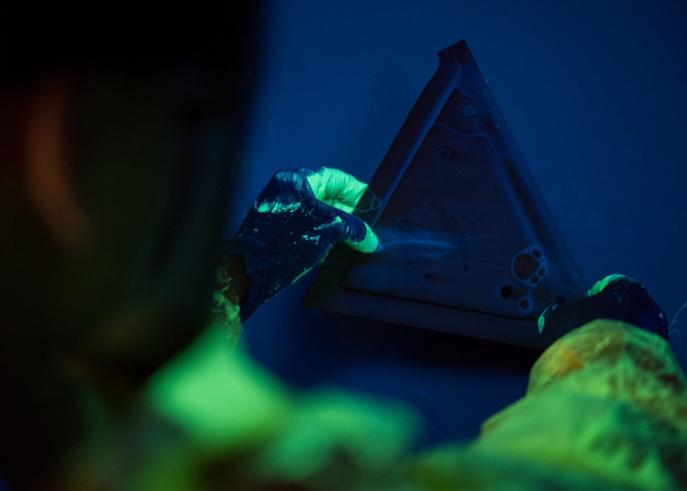 A Non-Destructive Inspection Airman dips an aircraft part into fluorescent penetrant at Whiteman Air Force Base