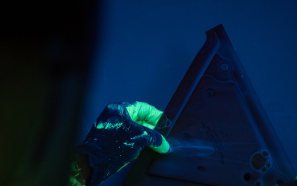 A Non-Destructive Inspection Airman dips an aircraft part into fluorescent penetrant at Whiteman Air Force Base