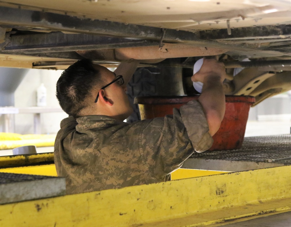 A wheeled vehicle mechanic changes the oil filter on a HUMVEE.