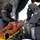A CBRN (Chemical, Biological, Radiological, Nuclear) training exercise is underway inside a field decontamination tent. Personnel wearing full protective suits and gas masks are practicing medical decontamination procedures on a training mannequin placed on a yellow stretcher. This appears to be a military or emergency response drill simulating casualty decontamination.