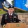 A U.S. Army officer in dress uniform is speaking at a podium during what appears to be a formal military ceremony. The officer's name tag reads 'KNIGHT' and he is wearing a black beret with a star insignia, along with multiple service ribbons and medals. Two military flags are visible in the background.