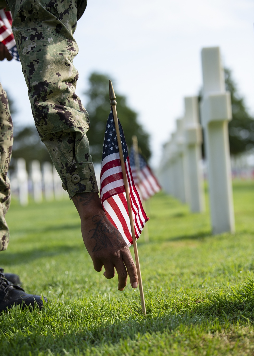 Sailor places flag on graves at the Normandy American Cemetery and Memorial.