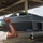 A ground crew member wearing hearing protection is signaling with hand gestures to a pilot seated in the cockpit of an F-22 Raptor stealth fighter jet inside a military hangar. The aircraft is gray and bears visible markings including a tail number and unit insignia. The scene appears to depict a pre-flight or taxi marshaling operation.
