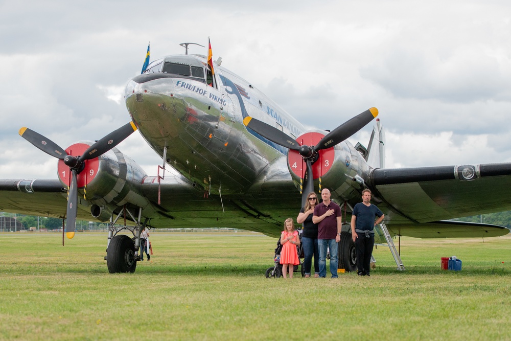 A family honors the playing of the U.S National Anthem in front of a Dakota DC3 Aircraft