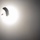 A silhouetted parachutist is captured mid-descent against a bright, overexposed sun in an otherwise hazy gray sky. The strong backlighting creates a dramatic contrast, rendering the parachute canopy and jumper as dark silhouettes. The image is shot from below, looking upward toward the subject.