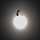 A silhouetted parachutist with a deployed canopy is captured against a large, bright circular light source — likely the sun obscured by haze or thin cloud cover. The image is shot from below, creating a dramatic backlit composition. The dark silhouette contrasts sharply against the glowing white orb in an otherwise gray, featureless sky.