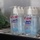 Multiple bottles of Purell Advanced Hand Sanitizer are displayed on a wire shelf, grouped in pairs and wrapped in plastic packaging. The bottles are the 8 fl oz (236 mL) size in the Refreshing Gel formula. The image appears to show a retail or supply storage setting with additional green items visible in the background.