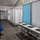The image shows a temporary or portable sanitation facility, likely a field hygiene station or emergency shelter bathroom area. It features a row of stainless steel sinks with faucets on a freestanding frame, alongside what appear to be portable shower or changing stalls. The structure is housed under a large tent or temporary enclosure with a white fabric roof.