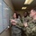 AFMES Joint MWD Lab ensures DoD kennels are meeting the standard Three military personnel from different branches of the U.S. armed forces are gathered around a large whiteboard reviewing what appears to be a tracking or scheduling chart. A female Air Force member is pointing at the board and holding a marker, appearing to brief or explain information to the other two. The group includes representatives from the U.S. Air Force, U.S. Army, and U.S. Navy, suggesting a joint military operation or coordination meeting.