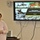 U.S. Transportation Command holds training on TMS prototype at Fort McCoy A woman is presenting in front of a wall-mounted Pioneer flat-screen television displaying a U.S. Army Logistics PowerPoint slide. The presentation title reads 'Data Capture TMS Prototype, Ft McCoy' with a date of 5-7 June 2013. The setting appears to be a conference or briefing room.