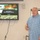 U.S. Transportation Command holds training on TMS prototype at Fort McCoy A middle-aged man in a blue plaid shirt is presenting in a conference or briefing room. Behind him, a wall-mounted Pioneer flat-screen television displays a U.S. Army Logistics presentation slide titled 'Data Capture TMS Prototype, Ft McCoy.' A whiteboard or flip chart is partially visible to his right.