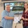 U.S. Transportation Command holds training on TMS prototype at Fort McCoy Two individuals are posing together while holding a certificate issued by the Transportation Management System (TMS) made out to 'Leslie Koenig.' The setting appears to be a conference or training room with a presentation displayed on a screen behind them reading 'Data Capture TMS Prototype, Ft McCoy.' The occasion appears to be a certificate presentation or award ceremony.