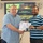 U.S. Transportation Command holds training on TMS prototype at Fort McCoy Two men are shaking hands while jointly holding a certificate in what appears to be a military or government training facility. The certificate appears to be issued to 'Anthony Reeves' from what reads as a Transportation Management System (TMS) program. A presentation screen in the background displays 'Data Capture TMS Prototype, Ft McCoy' with U.S. Army branding.