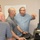 U.S. Transportation Command holds training on TMS prototype at Fort McCoy Four men are gathered around a computer workstation in what appears to be an office or training room setting. One man in a blue plaid shirt is pointing toward the monitor while another operates the keyboard, suggesting a demonstration or collaborative work session. A whiteboard with red writing is visible in the background.