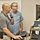 U.S. Transportation Command holds training on TMS prototype at Fort McCoy Two men are standing at a standing desk workstation in an office environment, appearing to review or discuss content on a computer monitor. The man in the foreground is operating a mouse while both direct their attention toward the screen. A whiteboard with handwritten notes is visible in the background.