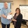 U.S. Transportation Command holds training on TMS prototype at Fort McCoy Two individuals are posing together while holding a certificate in what appears to be a training or conference room. The certificate appears to be issued by a Transportation Management organization and is made out to 'Nellie Pater'. Behind them is a whiteboard with URLs and numerical codes written on it, along with a monitor displaying a presentation.