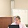 U.S. Transportation Command holds training on TMS prototype at Fort McCoy A woman in a light pink top is seated at a white table in what appears to be a meeting or training room, working on a black laptop while gesturing with her right hand. Behind her is a whiteboard on an easel displaying a numbered diagram with handwritten text. The setting suggests a professional training session, workshop, or committee meeting.