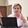 U.S. Transportation Command holds training on TMS prototype at Fort McCoy A middle-aged woman is seated at a desk with a laptop computer, actively speaking and gesturing with both hands raised. She appears to be presenting or explaining something in what looks like a classroom or conference room setting. A whiteboard with diagrams and text is visible in the background.