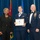 Airman Leadership School distinguished graduate A formal military graduation ceremony showing three individuals posing for a photo. The central figure, a female U.S. Air Force airman, is holding a framed diploma from the United States Air Force Airman Leadership School. She is flanked by a civilian woman in black attire on the left and a senior enlisted male officer (Chief Master Sergeant) in dress uniform on the right.