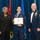 Airman Leadership School distinguished graduate A formal military graduation ceremony at the United States Air Force Airman Leadership School. A uniformed Airman holds a framed diploma issued to 'Sra Veronica M. Blanco,' flanked by a civilian woman in black attire and a senior enlisted military officer in dress uniform with medals. The backdrop features multiple flags including the U.S. flag and what appears to be the Jordanian flag.