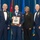 Airman Leadership School John L. Levitow Award Four individuals pose together at a formal military ceremony, with one junior enlisted airman holding a wooden plaque award. The setting appears to be an official Air Force awards ceremony, with multiple flags visible in the background including the U.S. flag and what appears to be the Jordanian flag. The award plaque features a portrait sketch and reads 'John L. Levitow Award'.