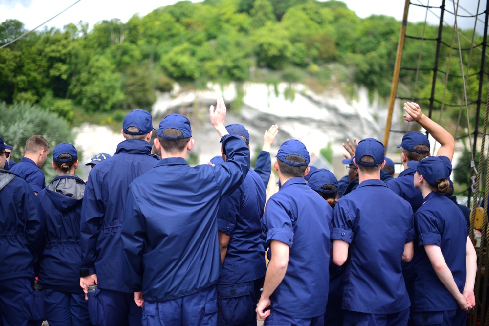 Coast Guard Cadets aboard the U.S. Coast Guard Tall Ship Eagle wave to crowds of people in France