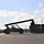 Fort McCoy supports USTRANSCOM's TMS prototype operations A large reach stacker or container handler vehicle is operating in what appears to be a military logistics or storage yard, maneuvering between rows of shipping containers. The vehicle is captured in near-silhouette against a partly cloudy sky, with its boom arm extended. The facility features multiple intermodal containers, light poles, and a paved surface consistent with a military installation or freight depot.