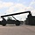 Fort McCoy supports USTRANSCOM's TMS prototype operations A large reach stacker or container handler vehicle is silhouetted against a partly cloudy sky, operating in what appears to be a military or industrial storage yard. The machine's extended boom arm is positioned over a shipping container on the right side of the frame. The strong backlighting creates a dramatic silhouette effect across the entire vehicle.