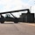 Fort McCoy supports USTRANSCOM's TMS prototype operations A large reach stacker or container handler vehicle is operating in what appears to be a military logistics or storage yard. The heavy equipment is silhouetted against a bright sky and is positioned near a row of shipping containers, suggesting active container handling or repositioning operations. The facility includes security lighting poles and appears to be a secured compound.