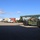 Fort McCoy supports USTRANSCOM's TMS prototype operations The image shows a logistics or intermodal yard with a military-olive green Kalmar reach stacker in the foreground, alongside a white semi-truck with a flatbed trailer. Multiple shipping containers of various colors are stacked in the background. The scene appears to depict container handling or loading operations at a freight or military logistics facility.