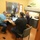 Fort McCoy supports USTRANSCOM's TMS prototype operations Three men are working together in a small office room. Two men are seated at a shared desk with a laptop and desktop monitor, appearing to collaborate, while a third man works independently at a separate workstation along the wall. The office is compact but functional, equipped with standard office furniture and equipment.