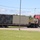 Fort McCoy supports USTRANSCOM's TMS prototype operations A dark red commercial semi-truck is hauling a flatbed trailer loaded with two large military-style containers or shelters. One container features a distinctive camouflage pattern (green, brown, and black), while the other is plain olive/gray. The scene appears to be at or near a military installation or logistics facility.