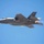 Red Flag 19-3 take offs A U.S. Air Force F-35A Lightning II stealth fighter jet is captured in flight against a clear blue sky. The aircraft bears the tail code 'WA', indicating assignment to Nellis Air Force Base, Nevada (57th Wing or USAF Weapons School). The engine is visibly firing with afterburner engaged, producing a bright flame and heat distortion at the exhaust nozzle.