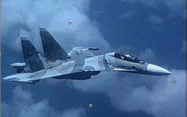 The image shows a military fighter jet, identifiable as a Sukhoi Su-30 variant, captured from another aircraft via what appears to be an electro-optical or surveillance camera system. The aircraft displays a two-tone camouflage paint scheme and has a visible tail number partially readable as '1167' or similar. The image contains targeting/tracking overlay markers typical of airborne surveillance or intercept camera systems.