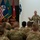 Paralegal training ensures disciplined forces are lethal forces A senior military officer in U.S. Army combat uniform (OCP/MultiCam) addresses a large group of seated soldiers in a formal briefing or town hall setting. The speaker is gesturing with both hands, suggesting an engaged presentation or speech. Multiple military flags are displayed in the background, indicating an official military venue.