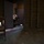 Paralegal training ensures disciplined forces are lethal forces A soldier in full combat gear and helmet is crouched in a doorway of an abandoned or training building, aiming a rifle into the room. The setting appears to be a military urban operations training facility, characterized by concrete block walls, a bare concrete floor, and minimal furnishings. The lighting is dramatic, with a shaft of light illuminating the soldier against the darker interior.